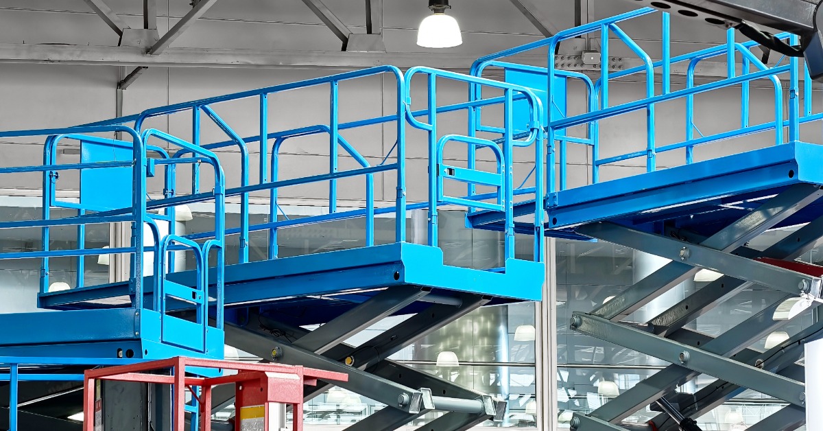Blue scissor lifts off to the side of a business warehouse. The lifts are slightly raised and there's nobody around.